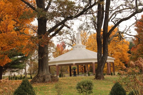 A gazebo surrounded by vibrant autumn trees with colorful leaves in a serene park setting.
