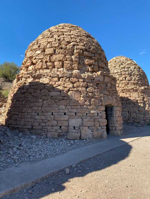 Two large stone kilns with dome-shaped roofs, set against a clear blue sky and rocky terrain.