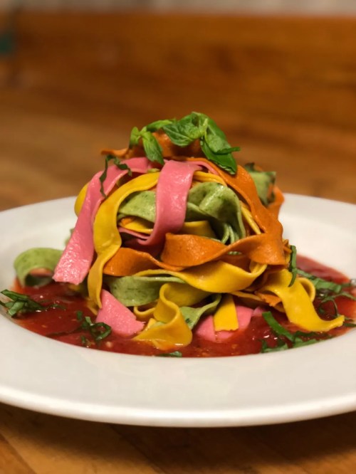 Colorful pasta ribbons in a vibrant sauce, garnished with fresh basil, served on a white plate.