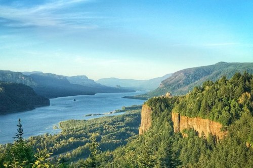 A scenic view of a river winding through lush green mountains under a clear blue sky.