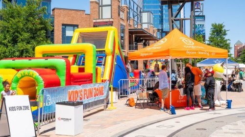 Colorful inflatable structures and a tent labeled "Kids Fun Zone" at a lively outdoor event. Families enjoy the activities.