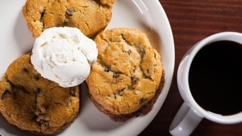 A plate of chocolate chip cookies topped with a scoop of ice cream, alongside a cup of black coffee.