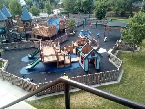 A colorful playground with slides, climbing structures, and playhouses, surrounded by grass and trees.