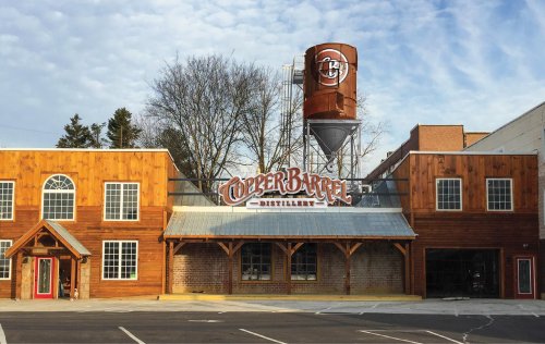 Exterior of Copper Barrel Distillery featuring wooden architecture and a water tower against a cloudy sky.