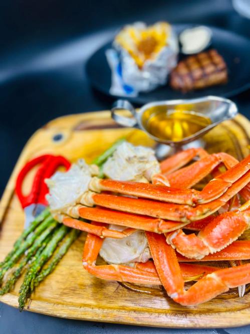 A wooden platter with steamed crab legs, asparagus, and a small bowl of melted butter.