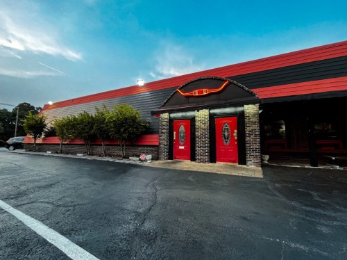 Exterior of a red and black building with two red doors, surrounded by trees and a cloudy sky.