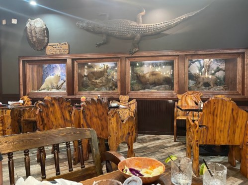 Interior of a rustic restaurant featuring wooden furniture, animal displays, and a large crocodile sculpture on the wall.