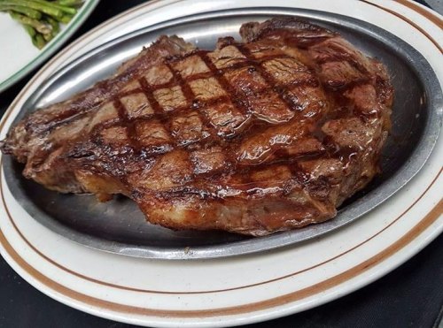 A perfectly grilled ribeye steak on a silver platter, showcasing a crosshatch sear and juicy texture.
