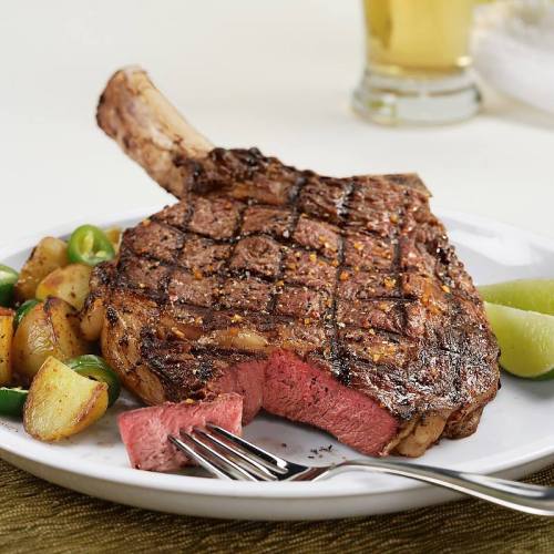 A perfectly cooked steak with a pink center, served with roasted potatoes and lime wedges on a white plate.