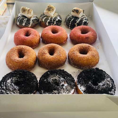A box of assorted donuts: some with chocolate and marshmallow toppings, others with red and black sprinkles.