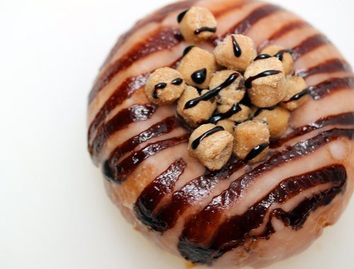 A glazed donut topped with chocolate drizzle and small cookie dough pieces.