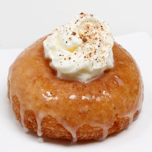 A glazed donut topped with whipped cream and a sprinkle of cinnamon.