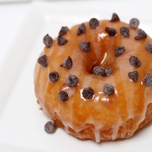 A glazed donut topped with chocolate chips, resting on a white plate.