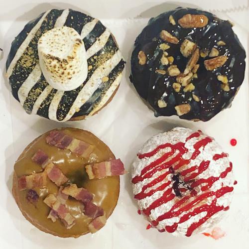 Four gourmet donuts: striped chocolate, chocolate with nuts, maple with bacon, and red velvet with icing.