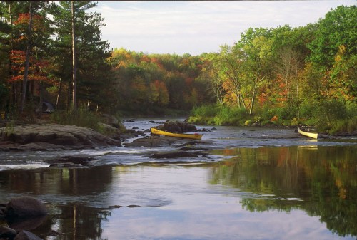 A serene river scene with two yellow canoes, surrounded by colorful autumn foliage and calm water reflections.