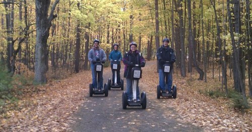 Four people riding Segways on a forest path surrounded by autumn foliage.
