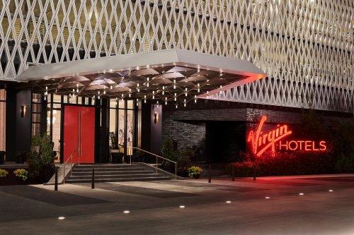 Entrance of Virgin Hotels featuring modern architecture and a glowing red sign.