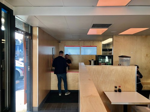Interior of a casual eatery with wooden walls, a counter, and two people interacting near the service area.