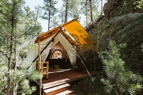 A cozy tent with a wooden deck nestled among tall trees and rocks in a serene outdoor setting.