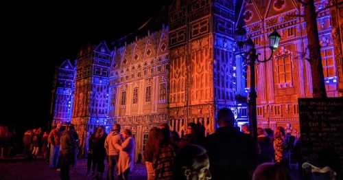 A brightly lit historic building at night, with colorful lights illuminating the facade and a crowd of people gathered below.