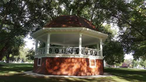 A wooden gazebo with a circular design, surrounded by lush green trees in a park setting.