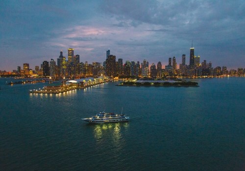 A boat sails on water near a city skyline at dusk, with lights reflecting on the surface and clouds in the sky.