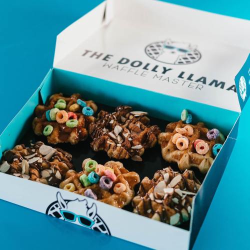 A colorful box of waffles topped with chocolate, nuts, and cereal, set against a bright blue background.