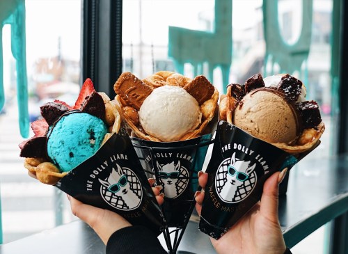 Three colorful ice cream cones with various flavors and toppings, held up against a window backdrop.