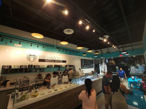 Interior of a vibrant café with a counter displaying desserts, customers ordering, and a modern, colorful design.
