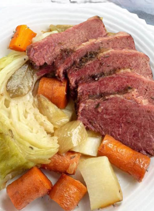 Sliced corned beef served with carrots, cabbage, and potatoes on a white plate.