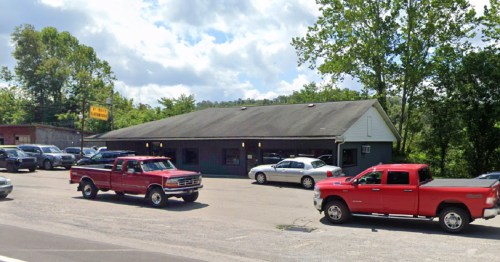 A parking lot with several cars, including two red pickup trucks, in front of a building surrounded by trees.