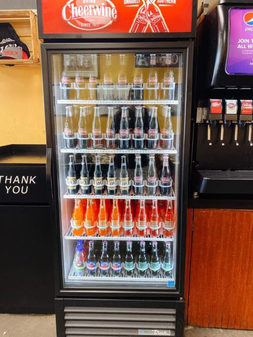 A vending machine filled with various bottles of Cheerwine and other soft drinks, displayed behind glass.