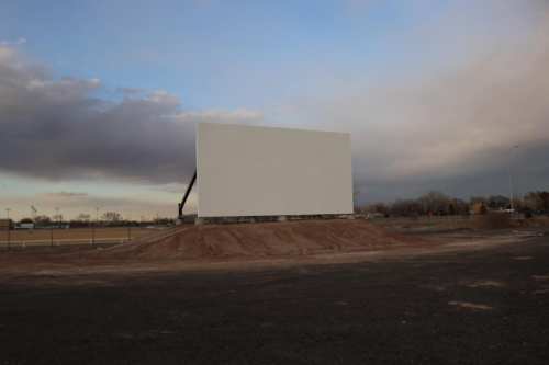 A large blank billboard stands on a dirt mound against a cloudy sky.