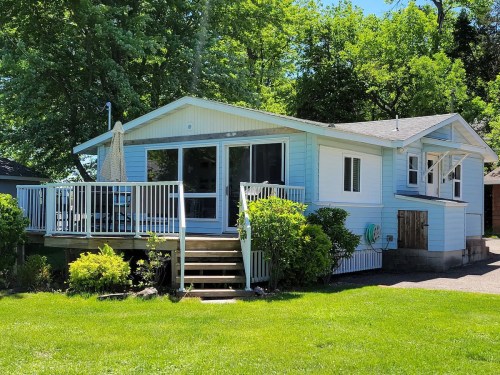 A light blue house with a deck, surrounded by greenery and trees, on a sunny day.