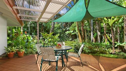 A shaded patio with a round table and chairs, surrounded by lush greenery and tropical plants.