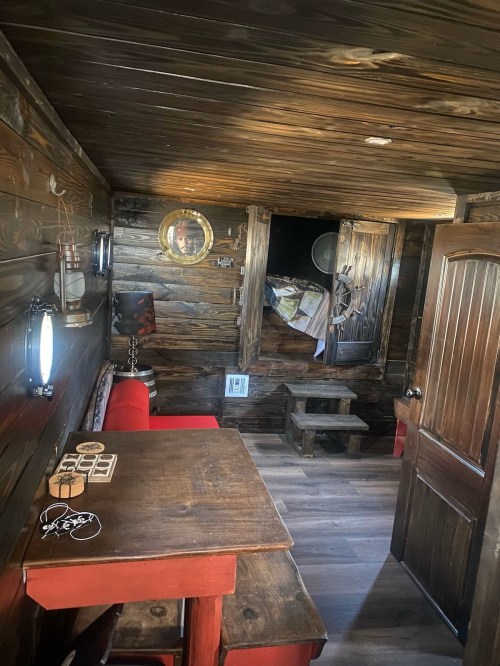 Cozy wooden interior of a small cabin, featuring a table, red couch, and a lofted sleeping area.