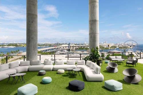 Modern outdoor lounge area with plush seating, green grass, and a view of the waterfront and city skyline.