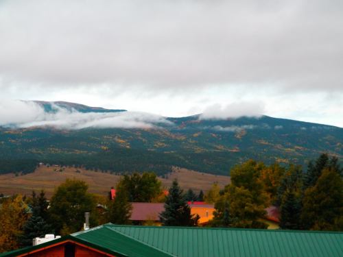 A scenic view of mountains with clouds, surrounded by trees and colorful autumn foliage under a cloudy sky.