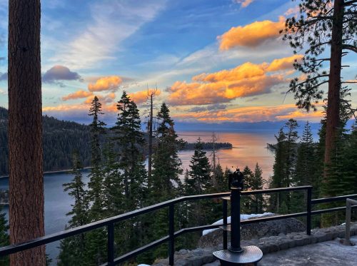 A scenic view of a lake surrounded by trees, with a colorful sunset and clouds reflecting on the water.