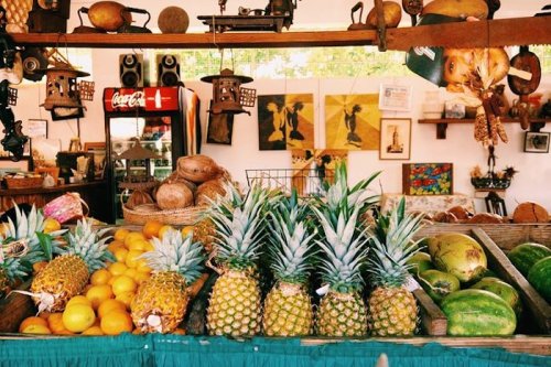 A vibrant market display featuring pineapples, oranges, and watermelons, with vintage decor in the background.