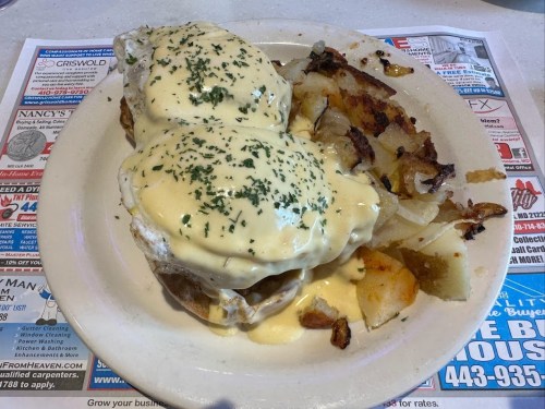 A plate of eggs Benedict topped with hollandaise sauce, served with crispy potatoes on the side.