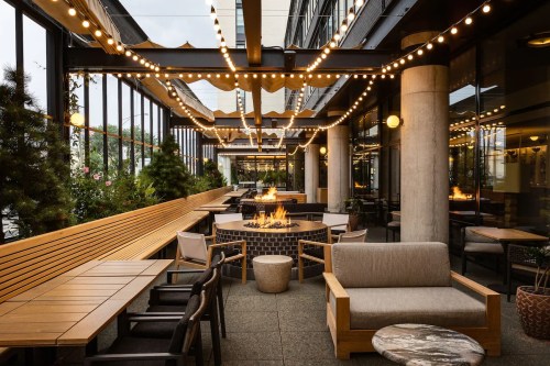 Cozy outdoor seating area with string lights, a fire pit, and greenery, creating a warm and inviting atmosphere.