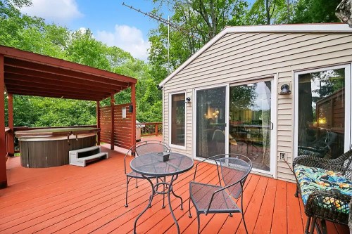 A cozy outdoor deck with a hot tub, seating area, and lush greenery in the background.