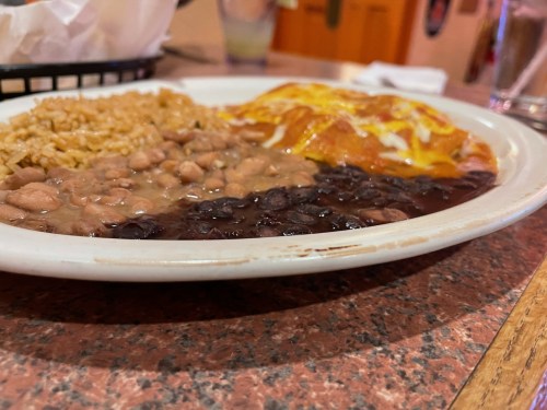 A plate of Mexican food featuring rice, refried beans, black beans, and a cheese-covered enchilada.