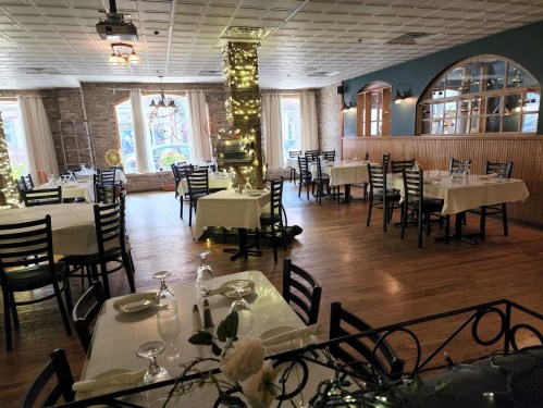 A cozy restaurant interior with tables set for dining, soft lighting, and a warm ambiance.