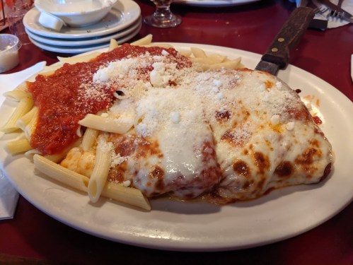 A plate of baked pasta topped with marinara sauce, melted cheese, and grated Parmesan, served with a knife.