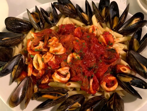A plate of pasta topped with seafood and marinara sauce, surrounded by mussels.