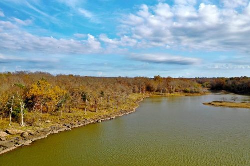 A serene landscape featuring a calm lake surrounded by trees and a blue sky with scattered clouds.