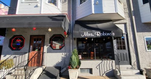 Exterior view of Mrs. Robino's restaurant, featuring a black awning and decorative lights, with steps leading to the entrance.