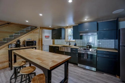 Modern kitchen with dark cabinets, stainless steel appliances, a wooden island, and a staircase in the background.